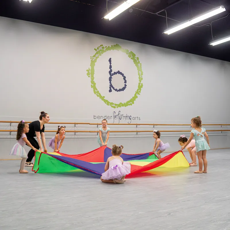 Young dancers and their teacher playing with a parachute.
