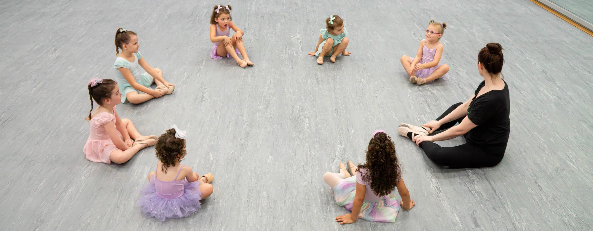 Young dancer sitting in a circle with their teacher.